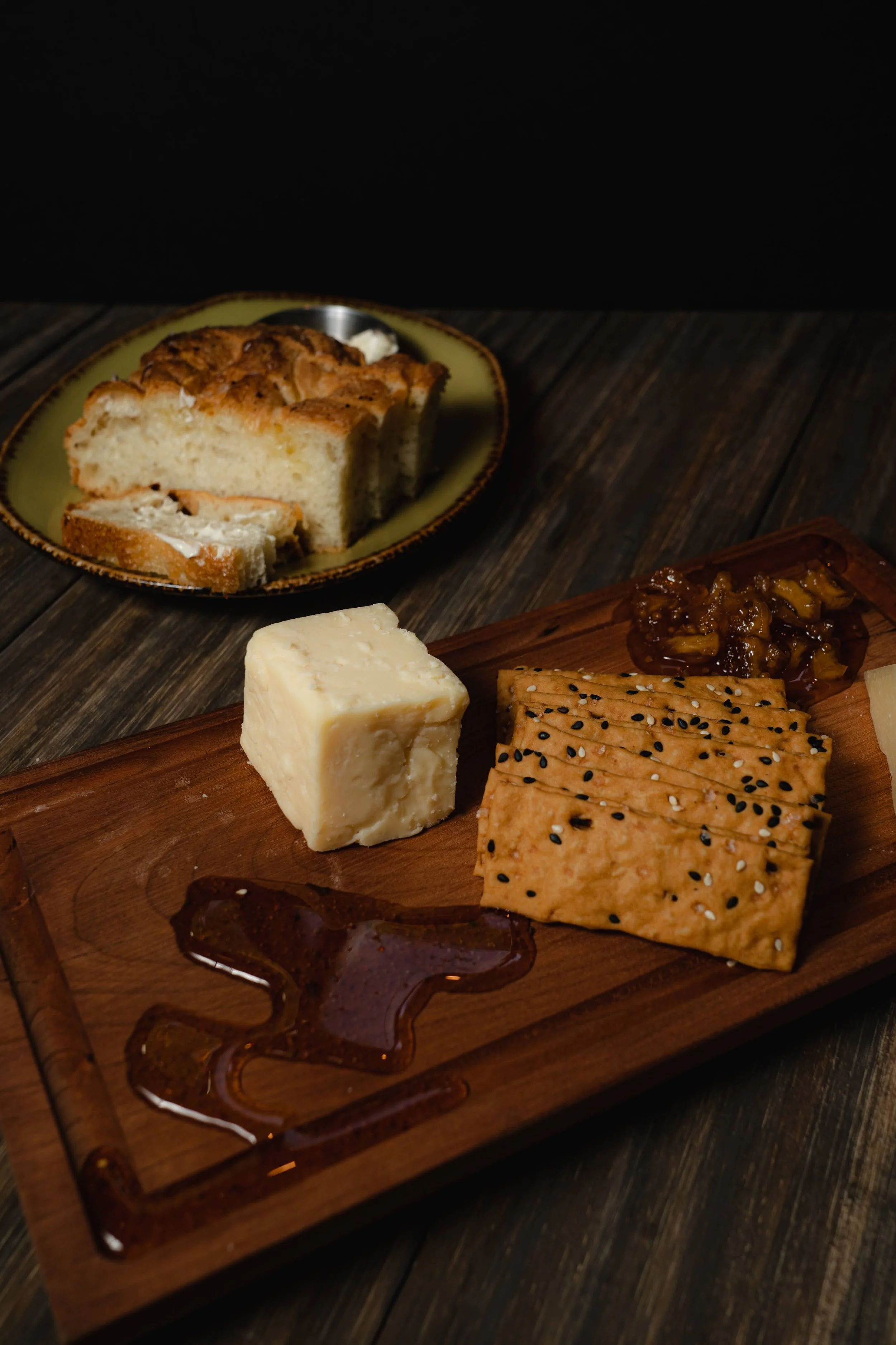 A cheese platter with various cheeses, crackers, and a small dish of caramelized onions on a wooden serving board.