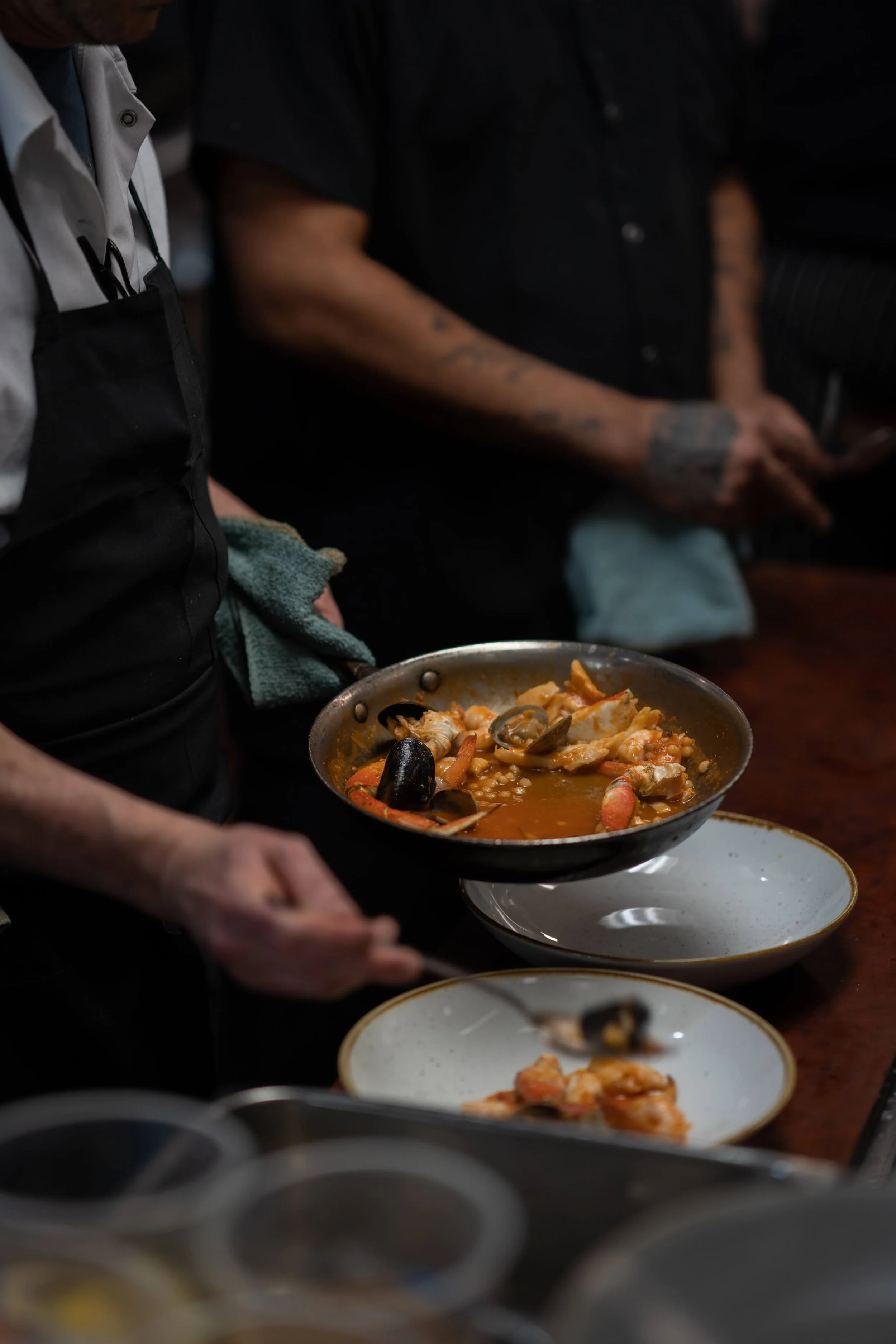People serving and preparing seafood paella in a kitchen setting.