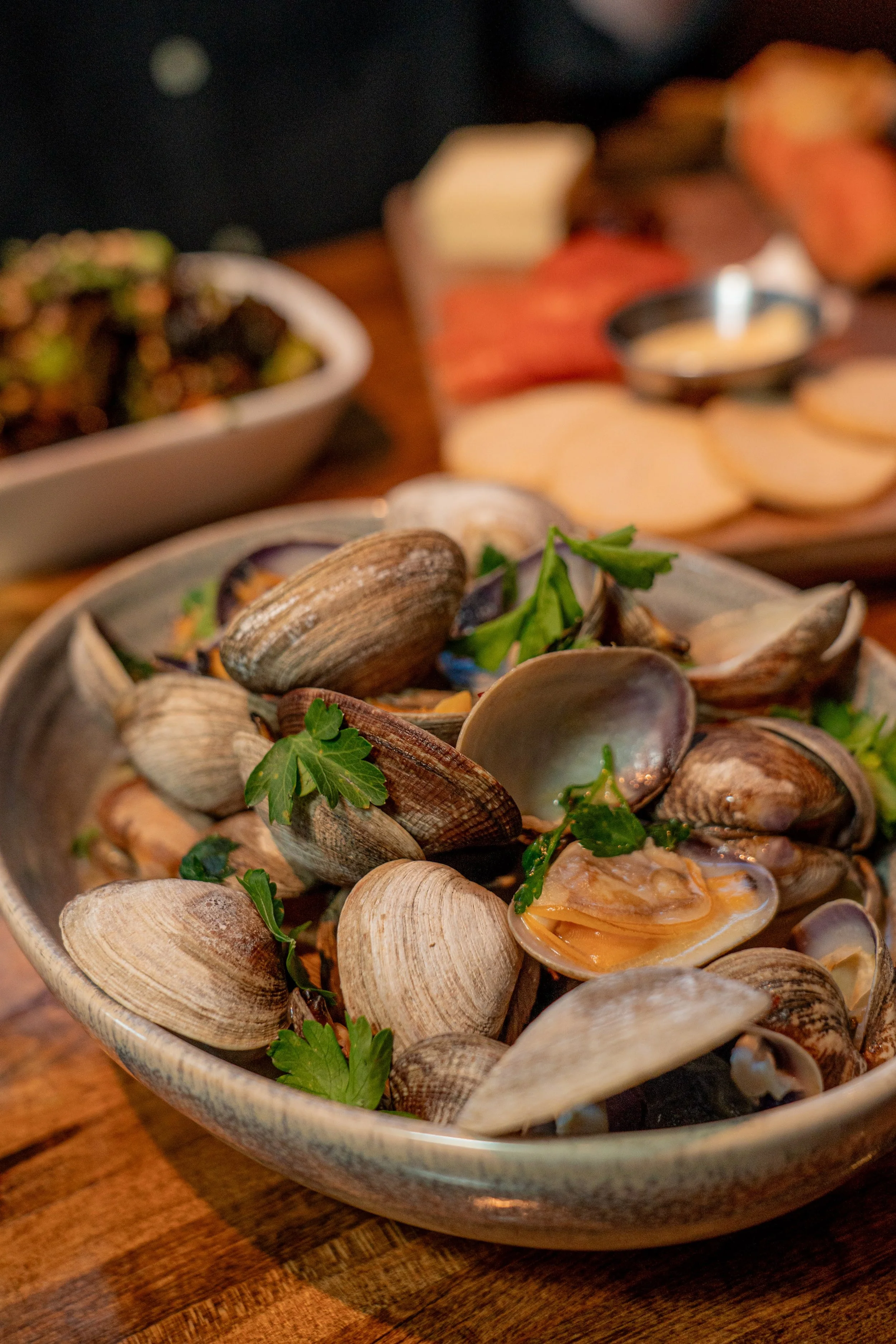 A bowl filled with cooked mussels garnished with parsley, placed on a wooden surface.