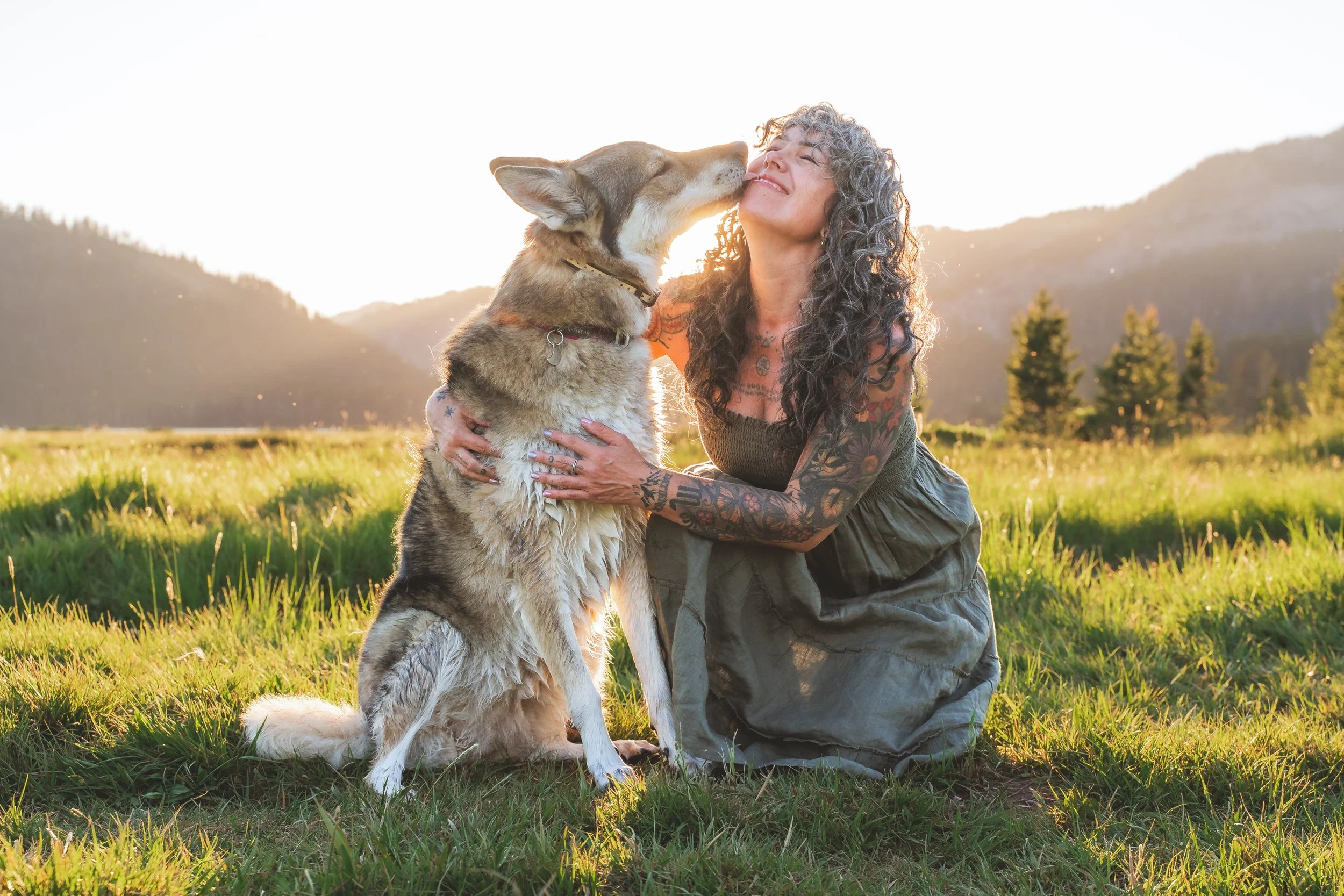 woman snuggles her dog in front of glowing hills at sunset.