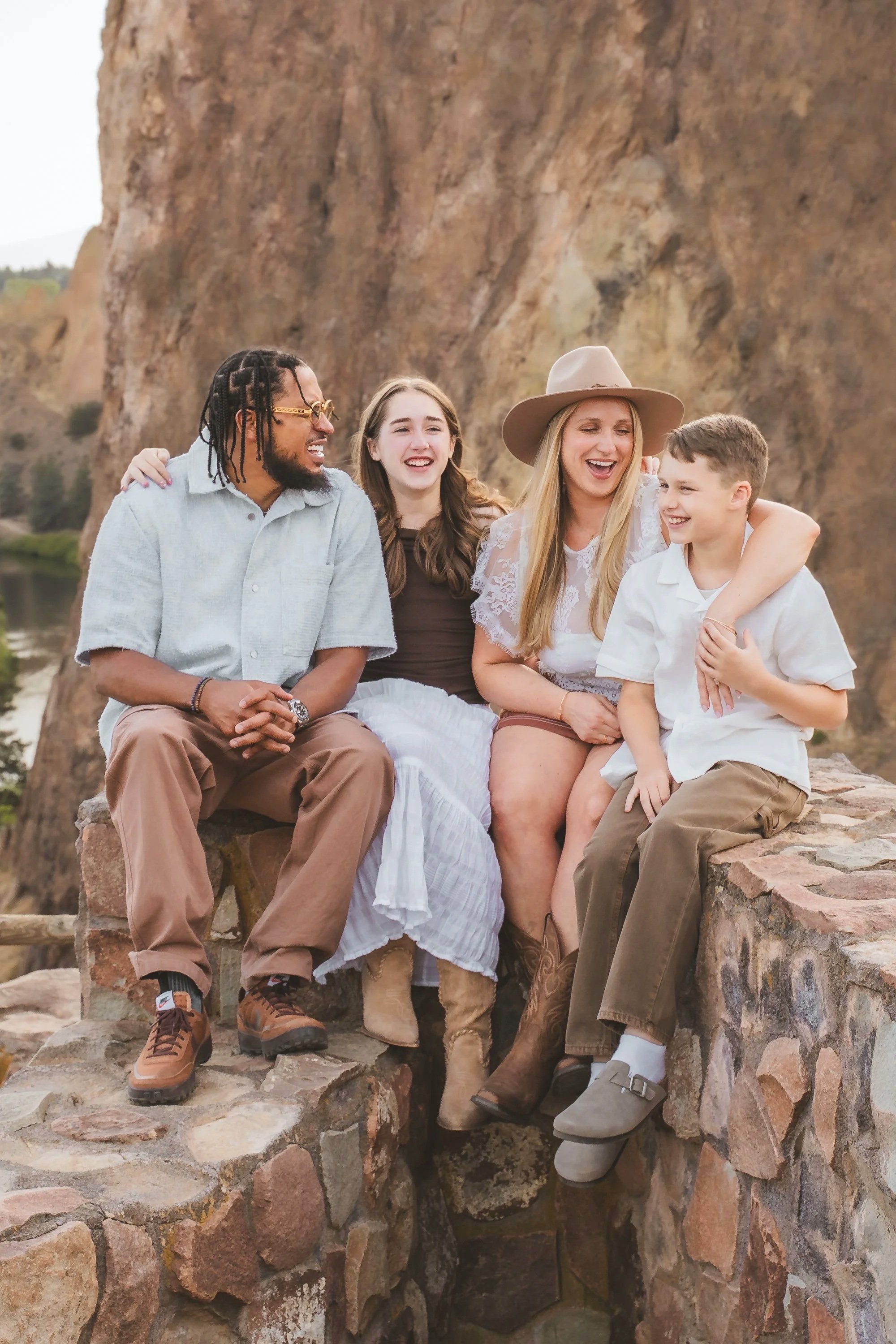 family of four snuggles on a rocky ledge. smith rock looms in the background.