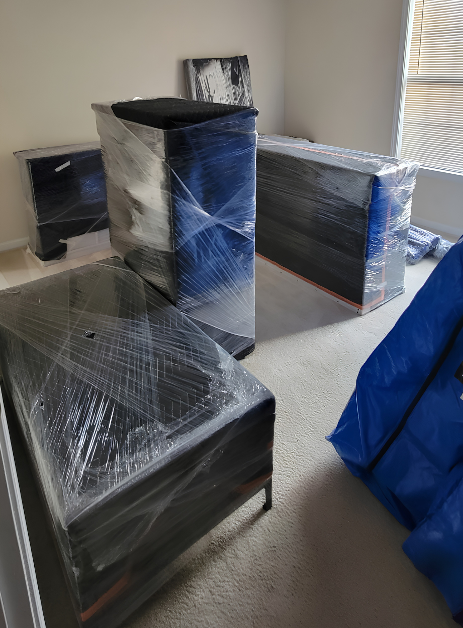 Furniture pieces wrapped in plastic in a room under moving or delivery.
