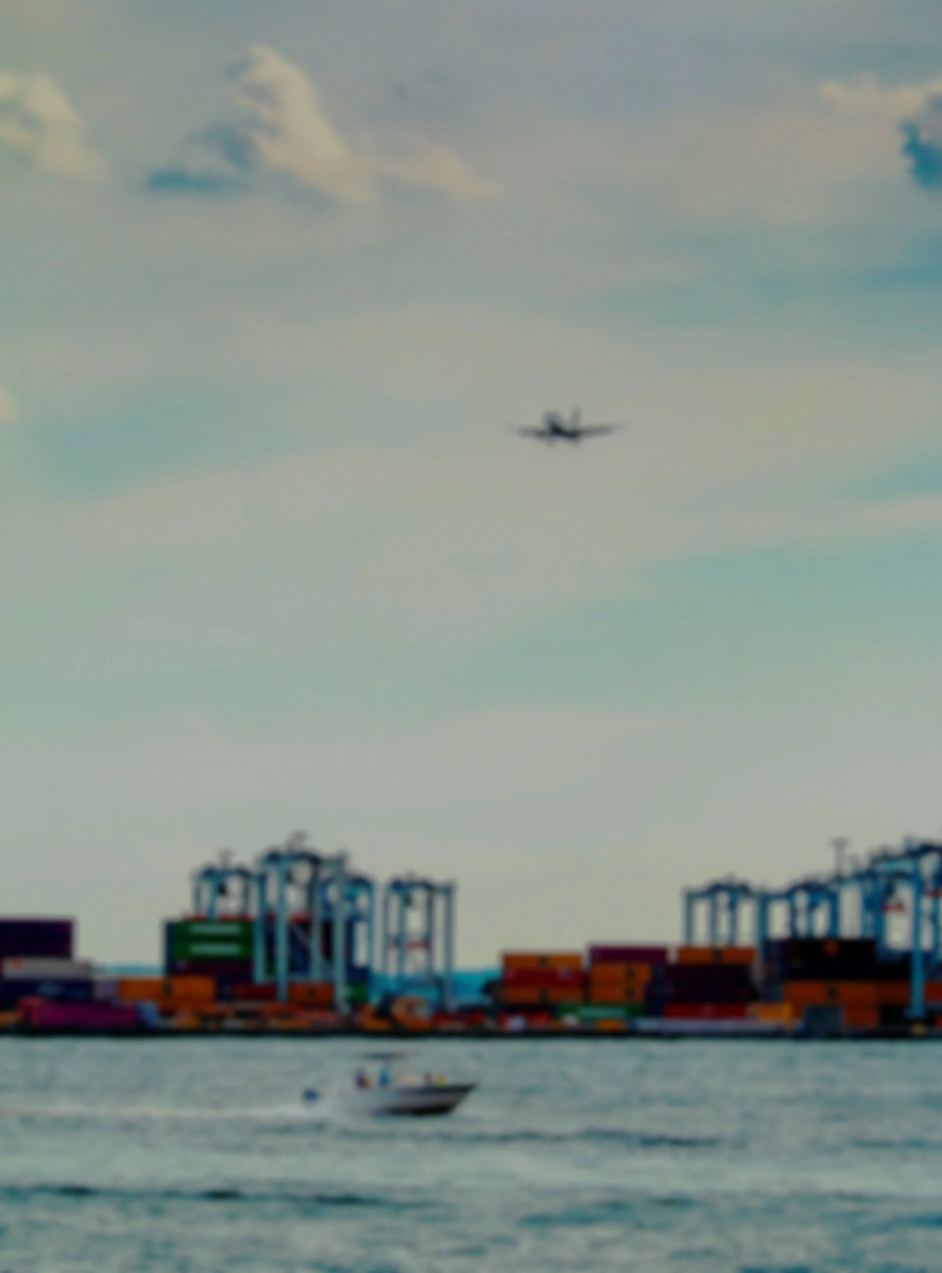 A large shipping container port on the water with colorful containers and a blurry cargo ship in the background, along with a boat on the water in the foreground.