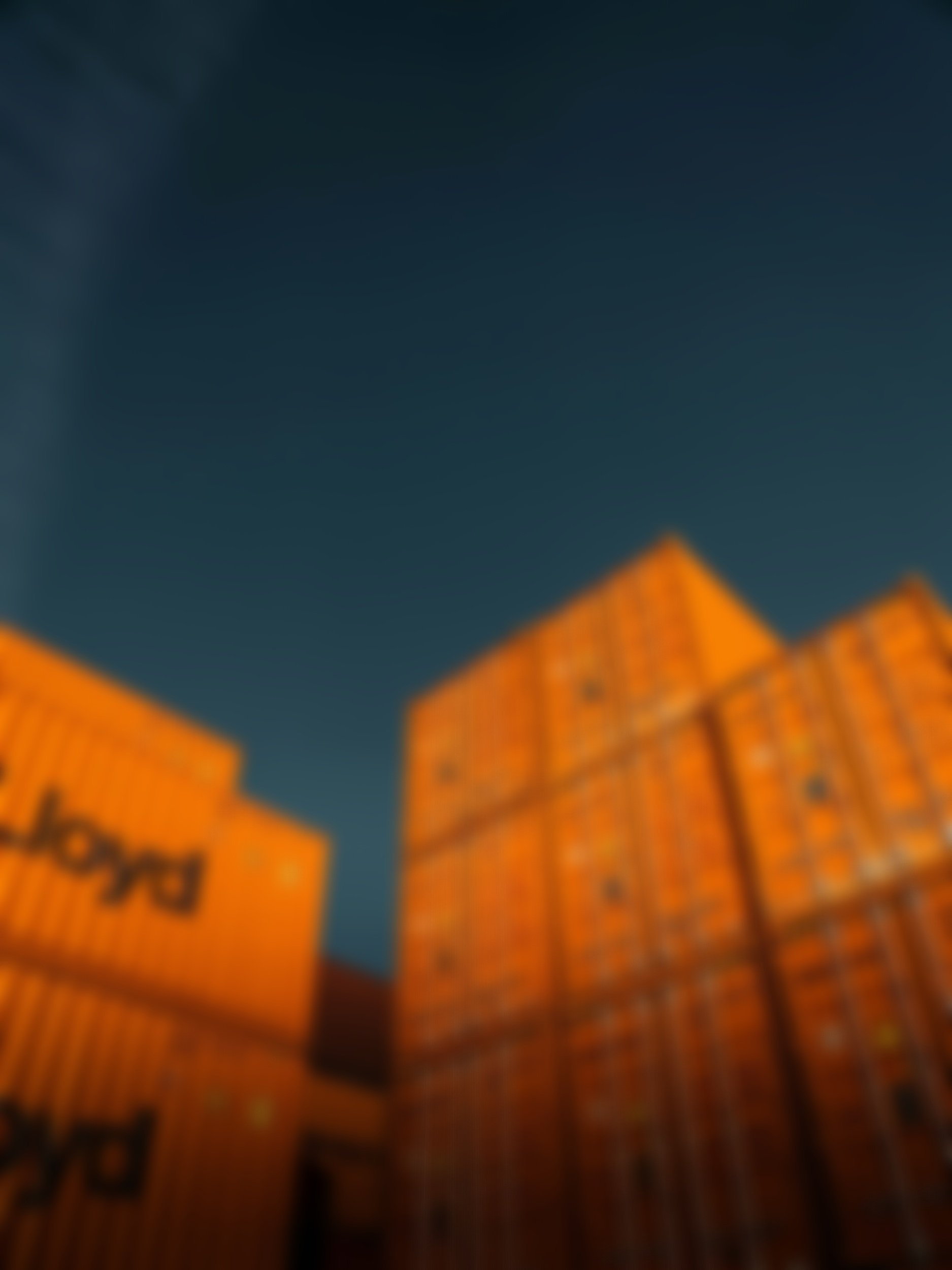 Blurred image of orange cardboard boxes with black symbols and text, set against a dark sky background.