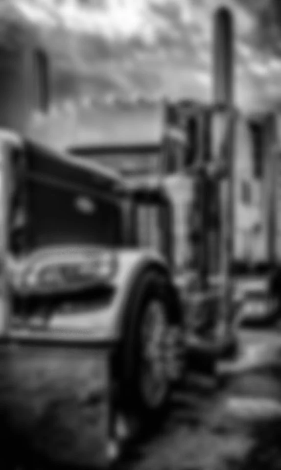 Black and white image of a semi-truck with a flatbed trailer carrying large objects, parked outdoors.