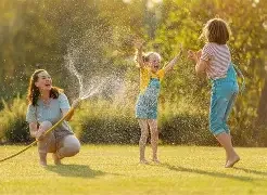Three young girls playing with a garden hose on a sunny day, spraying water and having fun in a grassy yard.