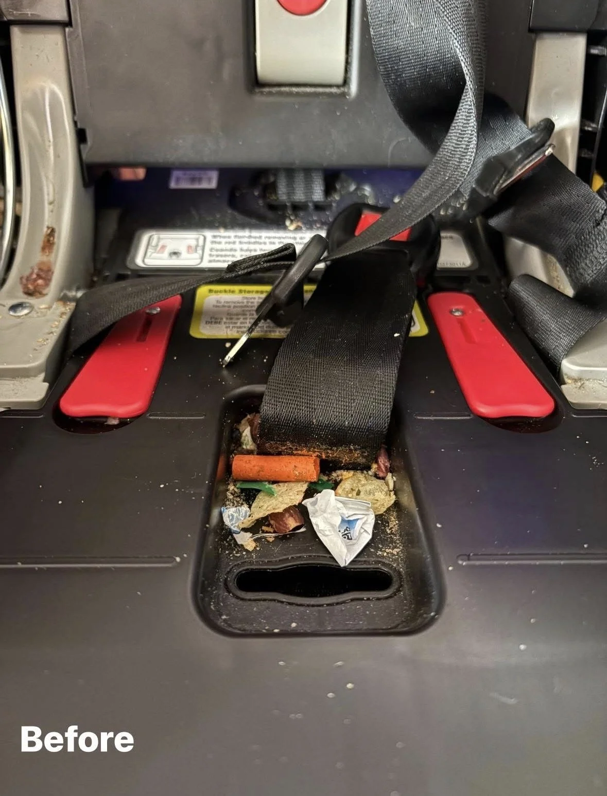 Close-up of a cluttered seat belt mechanism with trash and debris in the compartment below, dirt and dust visible around, and part of a vehicle's dashboard and seatbelt strap.
