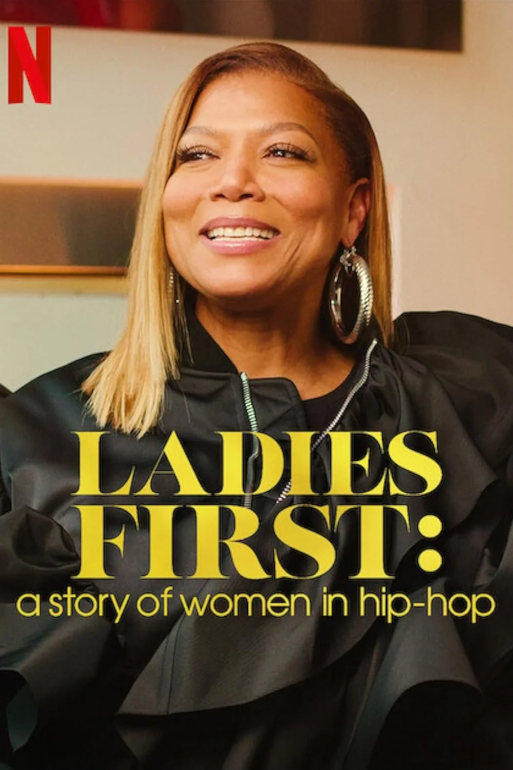 Queen Latifah smiling, wearing large hoop earrings and a black jacket, standing in front of a beige wall. The official poster for the Netflix original documentary series, "Ladies First: a story of women in hip-hop". Post Producer: Travis Preston