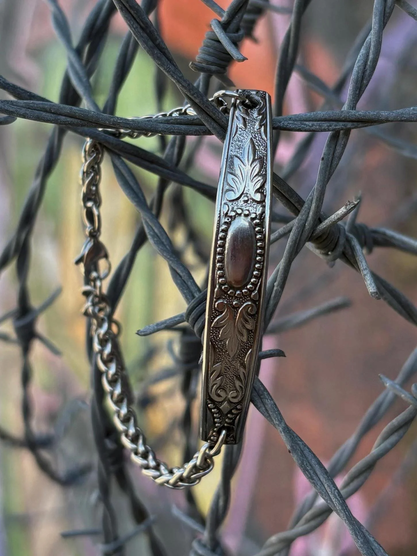 Close-up of a silver bracelet hanging on a rusty wire fence.