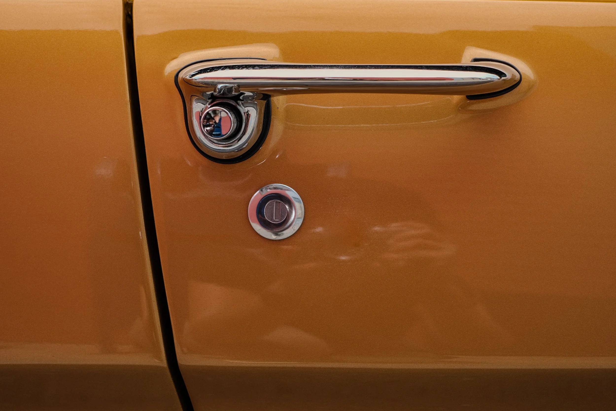 Close-up of a vintage car door handle and lock set on a mustard yellow car.