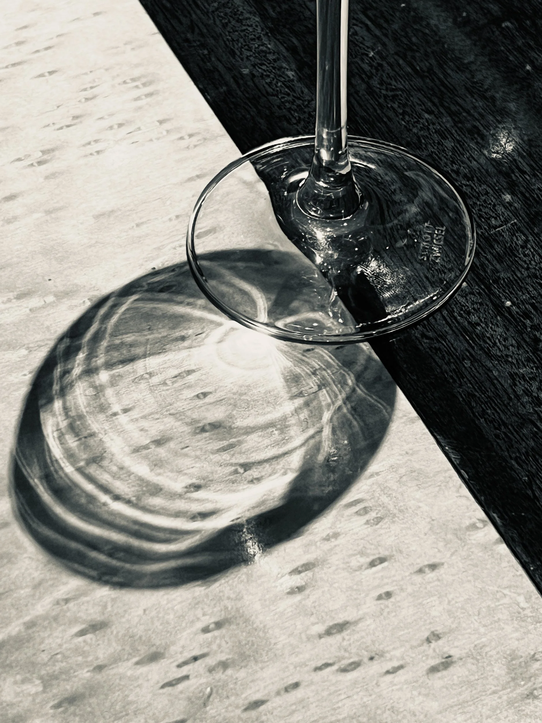Close-up of a wine glass on a textured table surface with shadows cast by the glass.