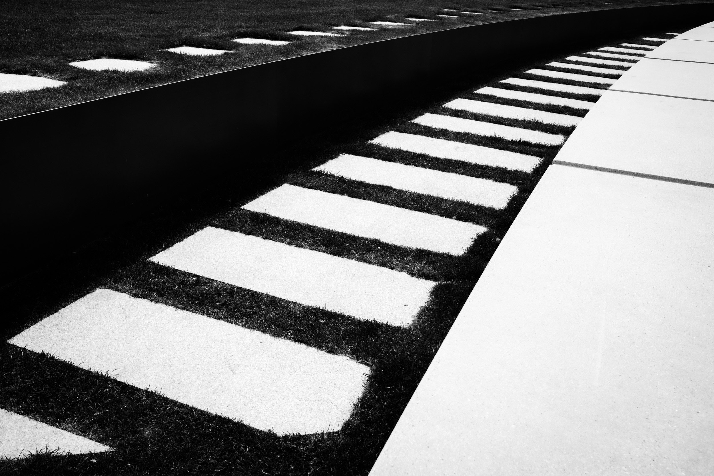 Black and white outdoor scene featuring intersecting concrete pathways with grass in between and a curved pathway on the right.