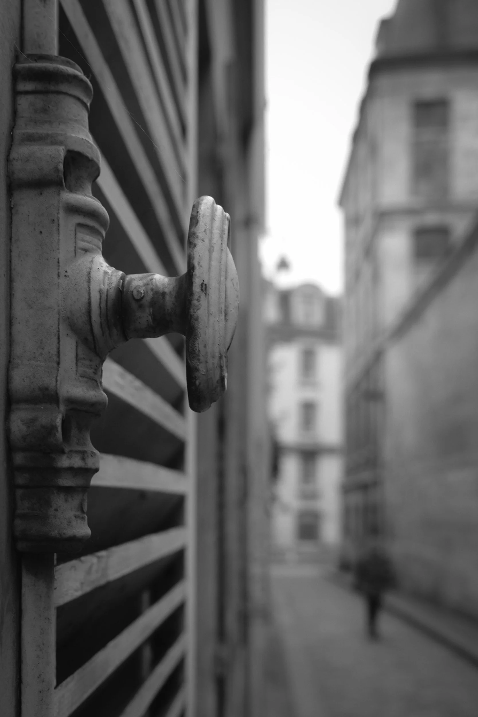Close-up of a metal outdoor faucet attached to a wooden slatted fence on a balcony, with buildings in the background.