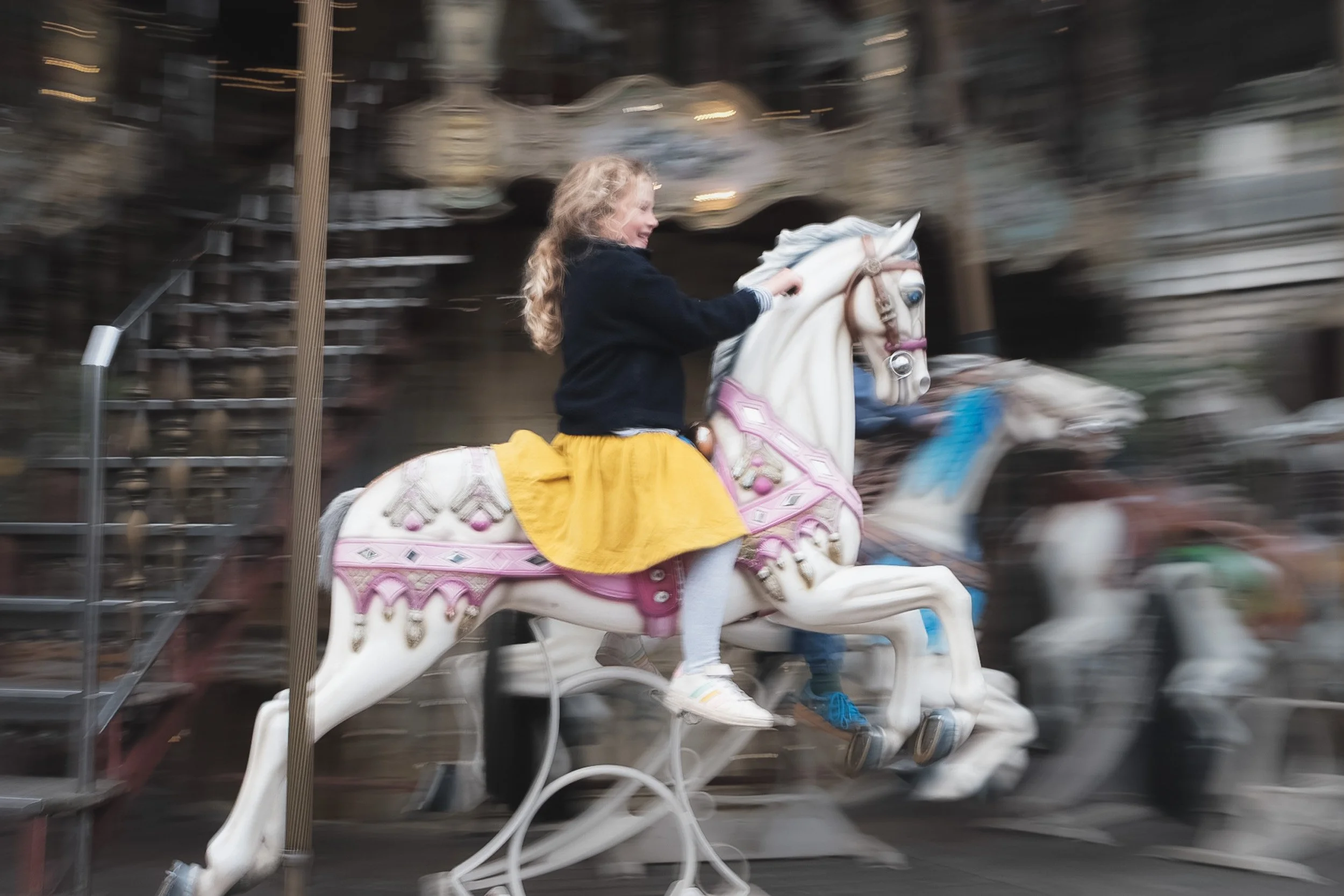 A young child riding a carousel horse in motion, with a blurred background indicating movement.