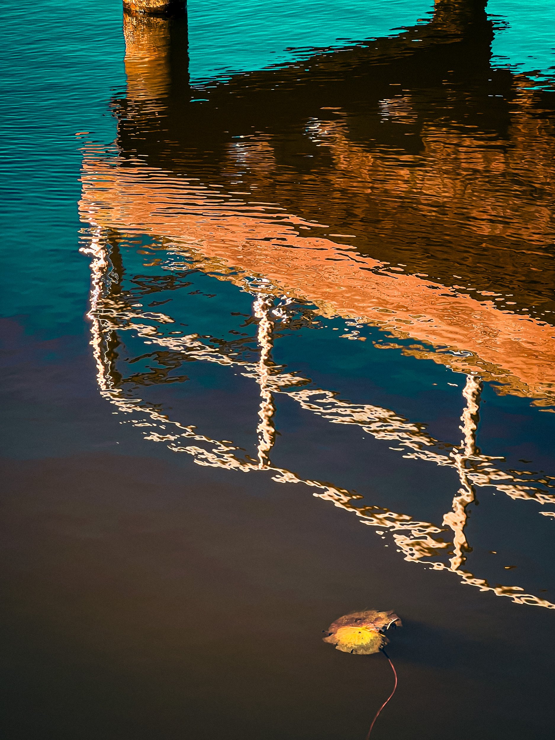 A reflection of a dock or pier with vertical posts in the water, illuminated with warm lights, and a floating leaf with a fishing line attached at the bottom of the image.