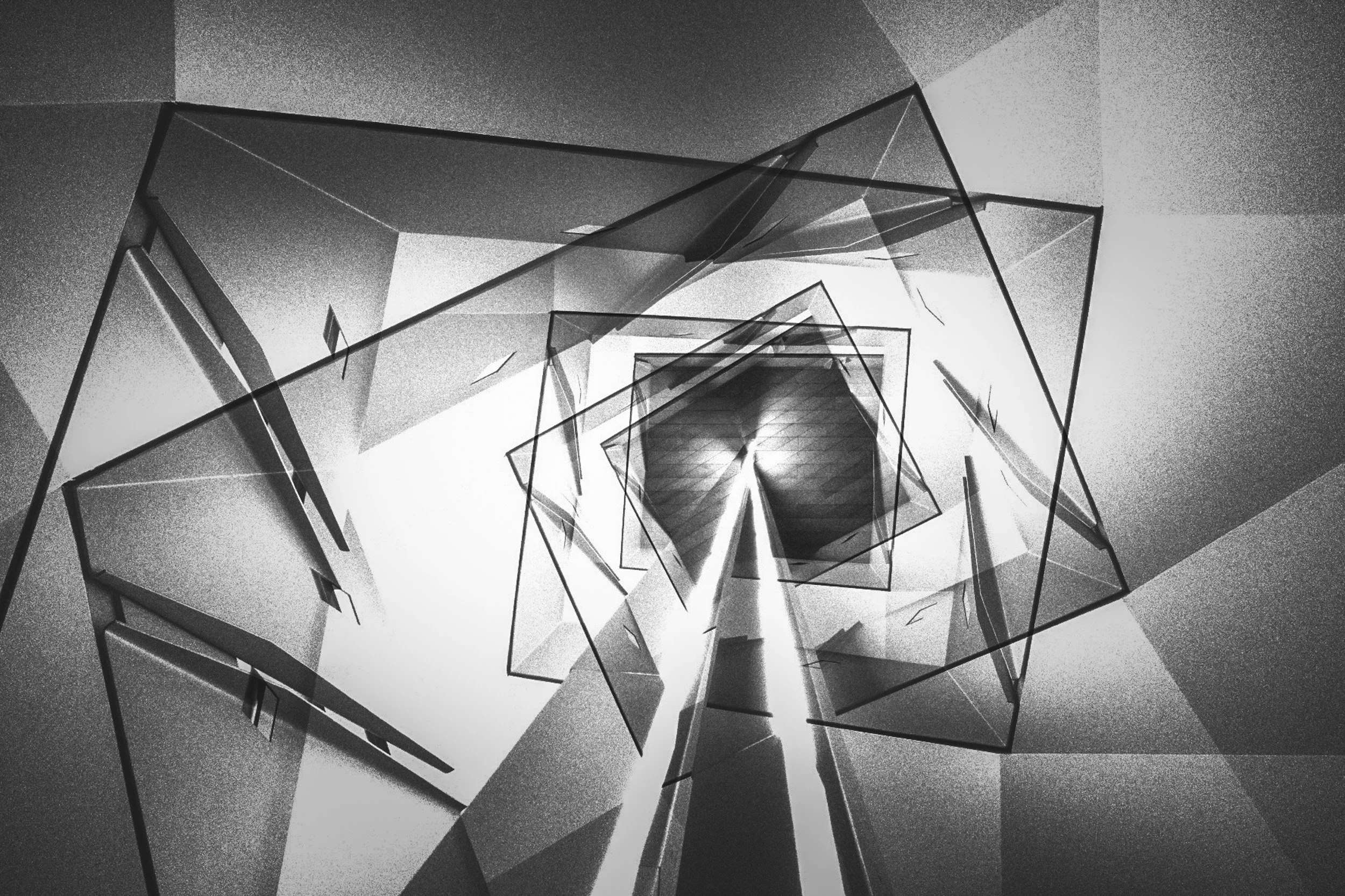 A black and white abstract photo of a modern staircase with glass and metal railings, seen from the bottom looking up.