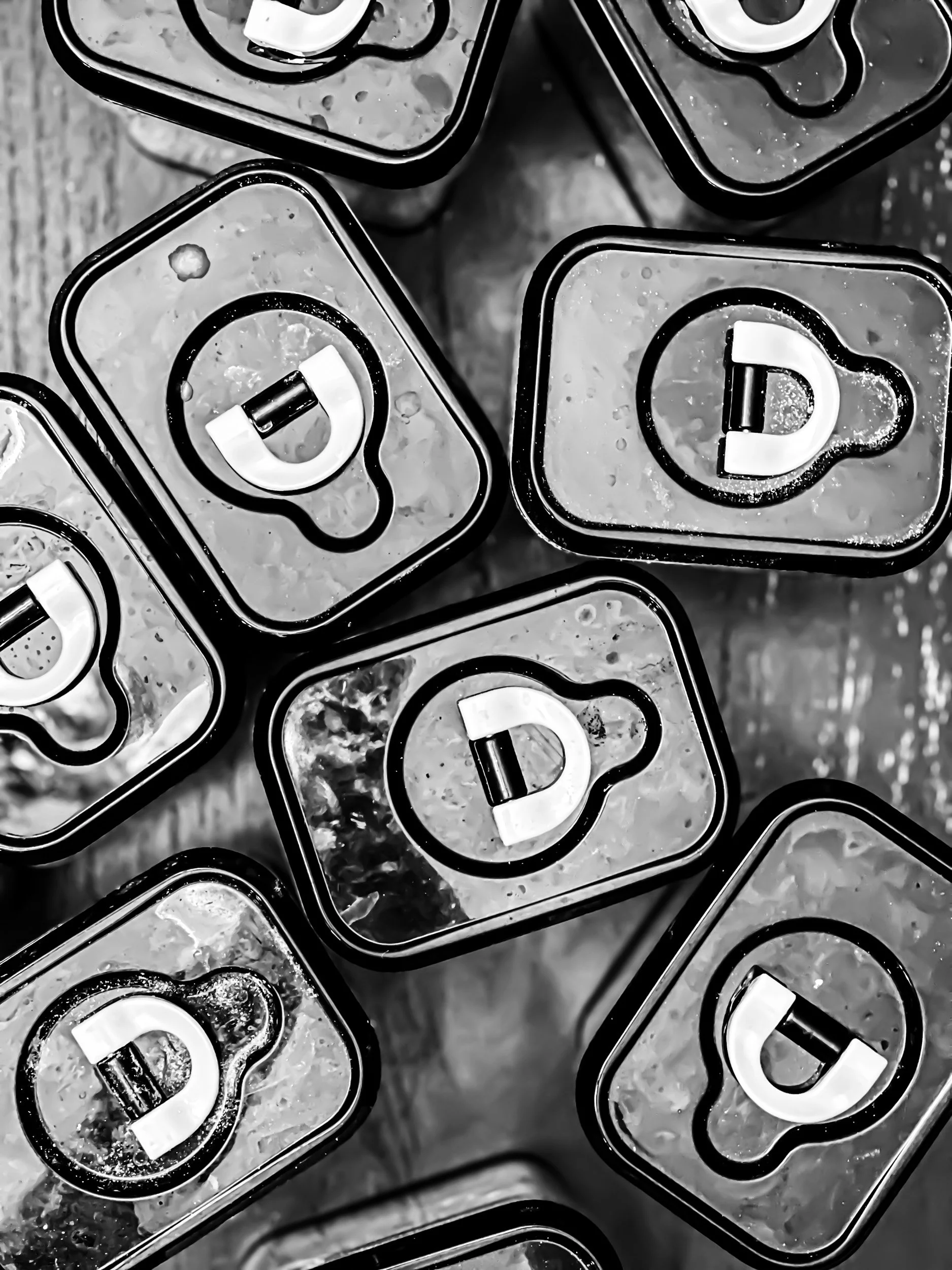 Close-up of soda cans stacked together, viewed from above, in black and white.