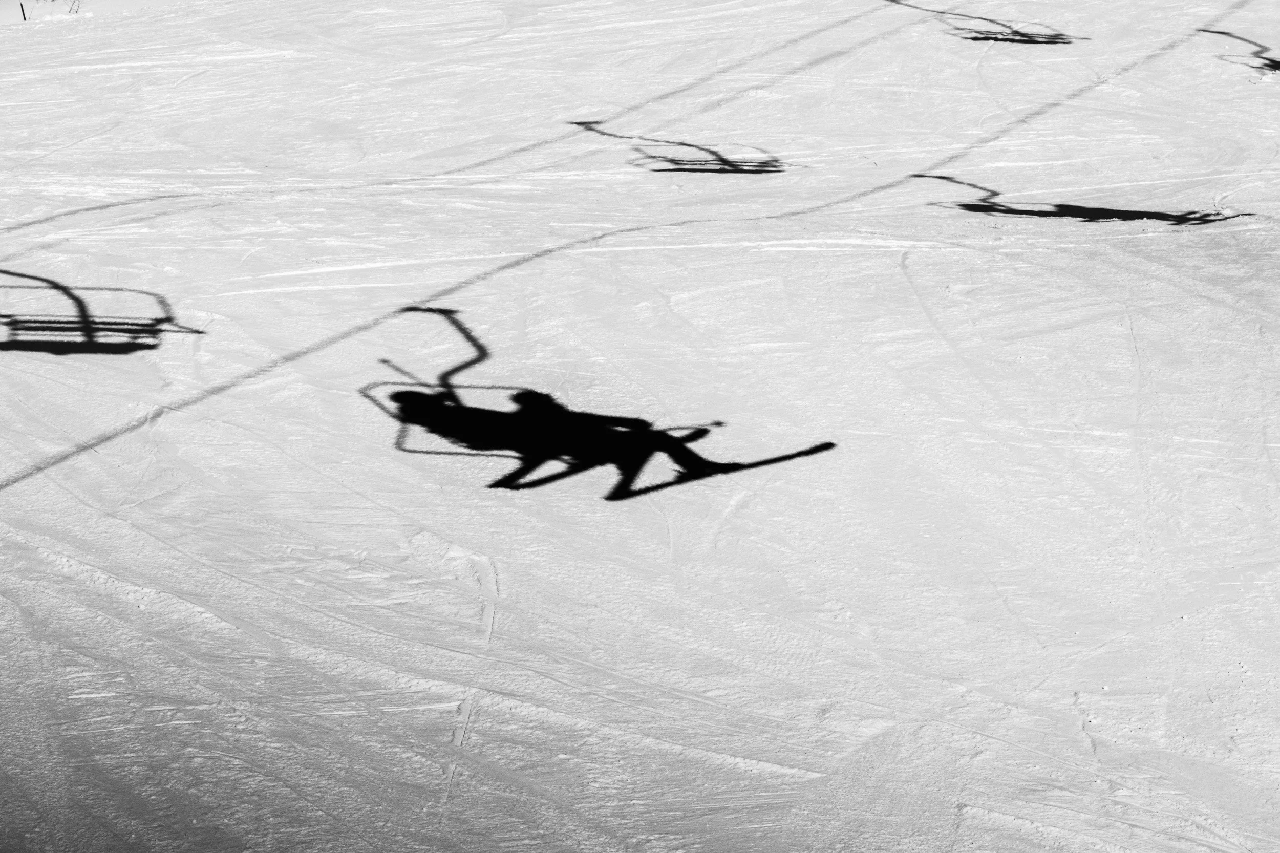 Shadow of a person skiing on snow, with ski poles, on a snowy landscape.