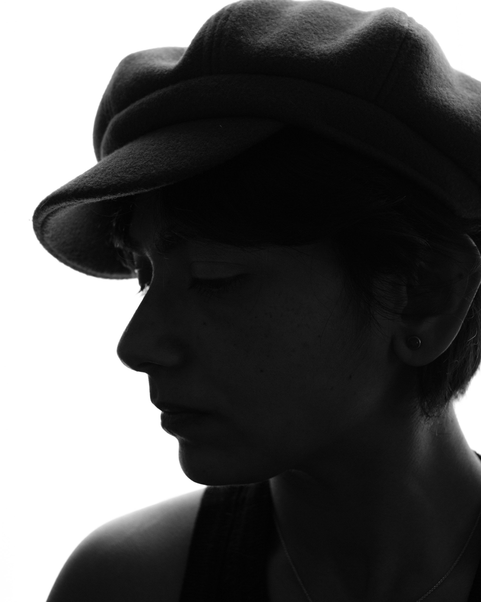 Side profile of a person wearing a fedora hat, with shadowed face and dark clothing.