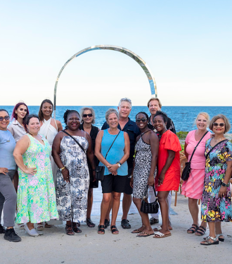 Group of people standing on a beach near a metalic arch on the beach.