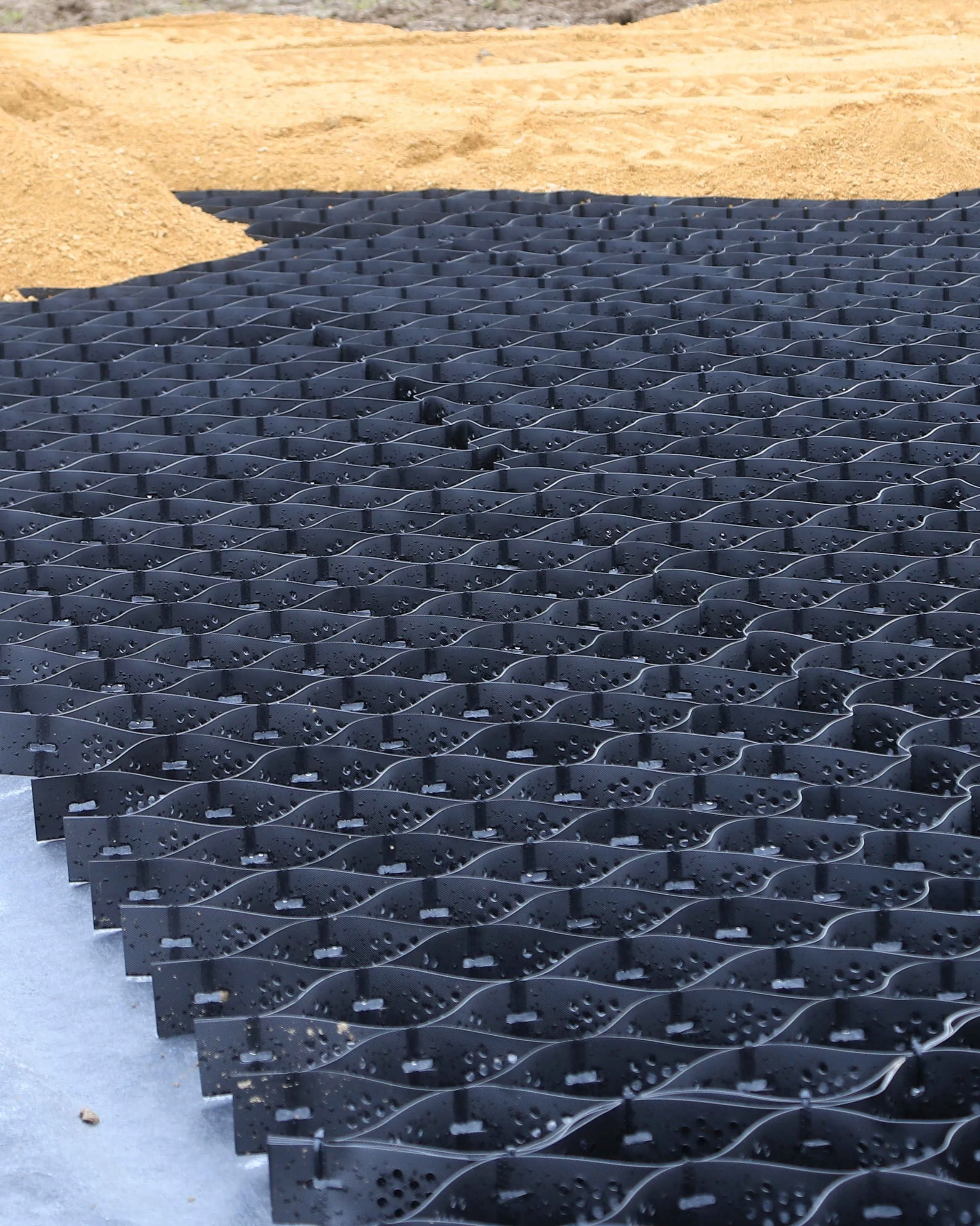 Géocellules alvéolaires posées sur géotextile, sable prêt à être épandu pour stabiliser le sol équestre