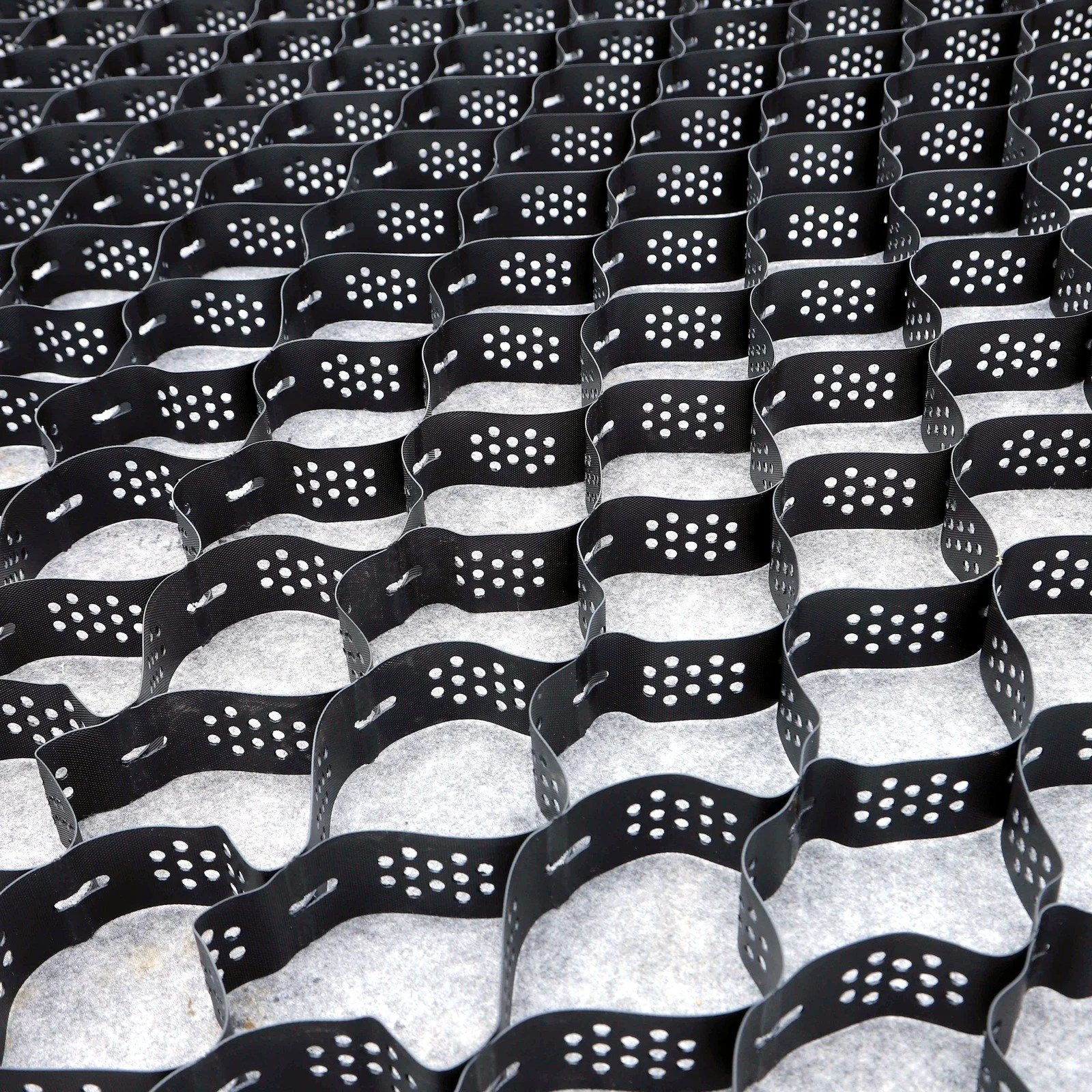 Dalles accordéon alvéolées noires empilées, utilisées pour stabiliser et drainer les sols équestres