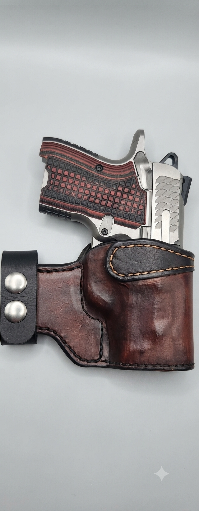 A semi-automatic handgun with a silver slide and black frame inside a brown leather holster with a strap and metal snaps.