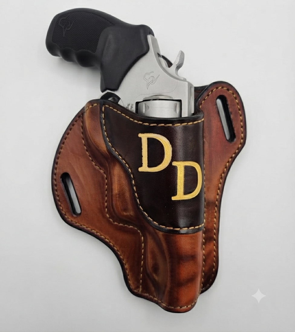 A silver revolver partially inside a brown leather holster with yellow stitched edges and two yellow embroidered 'D D' initials on the front, on a white surface.