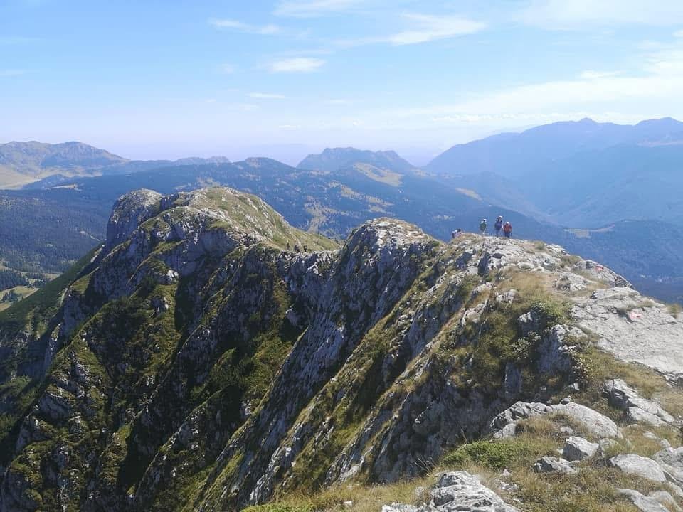 Mountain ridge with rocky peaks and grassy slopes, hikers standing on the top, in a scenic mountain landscape under a partly cloudy sky.