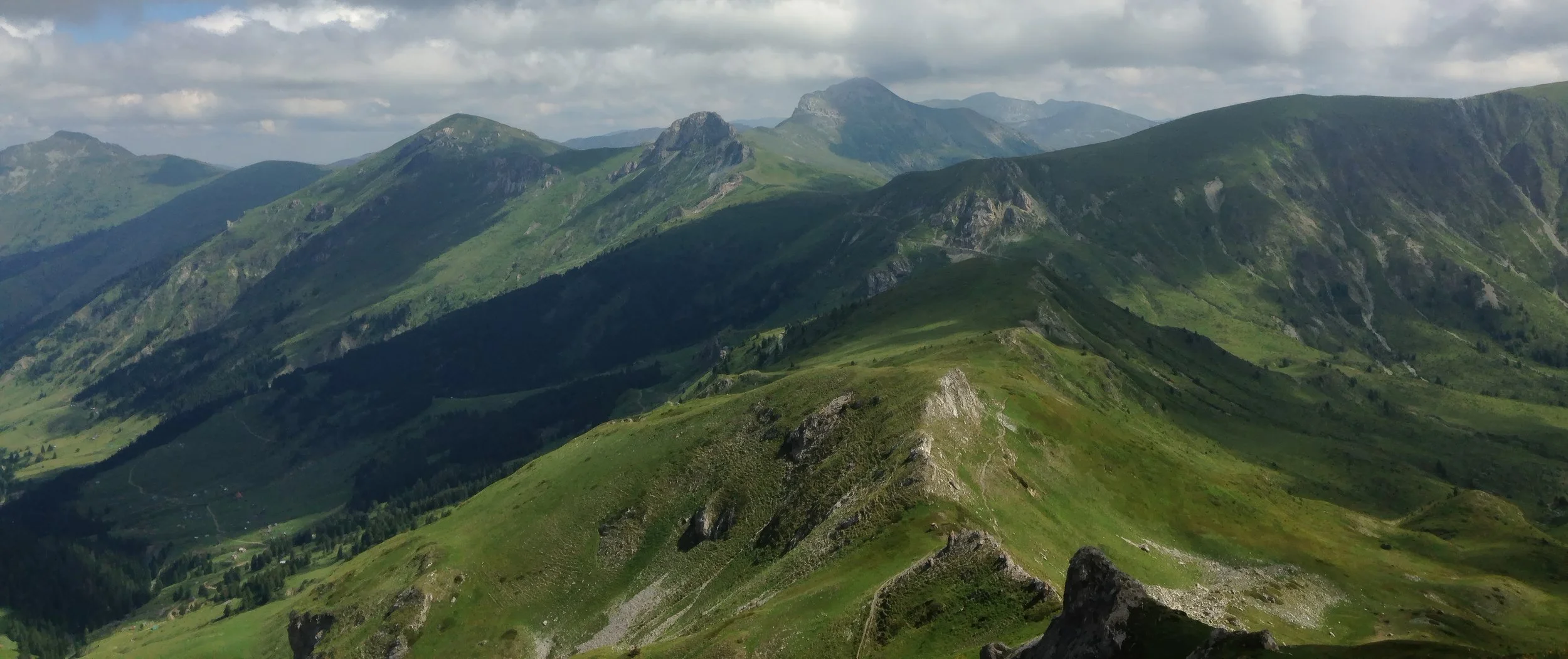 Green mountain landscape with slopes, peaks, and valleys under cloudy sky