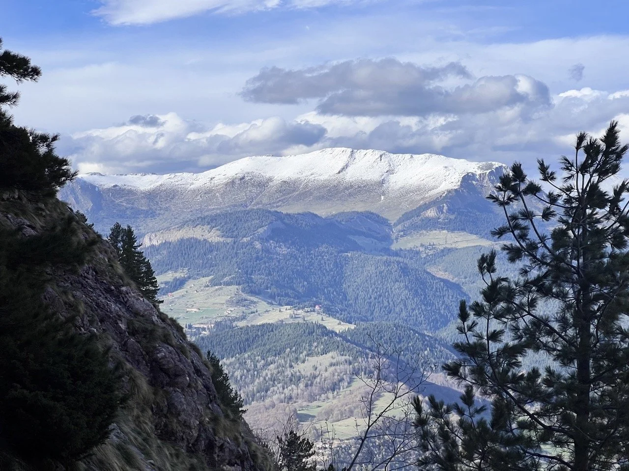 Mountain ridge with rocky peaks and grassy slopes, hikers standing on the top, in a scenic mountain landscape under a partly cloudy sky.