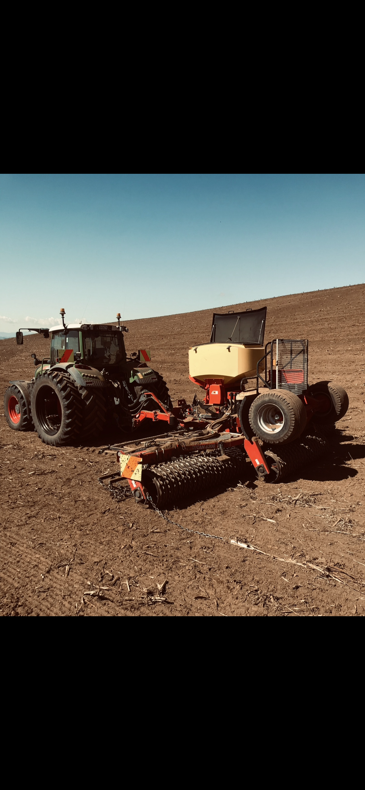 A tractor pulling a seeding drill on a bare dirt paddock.