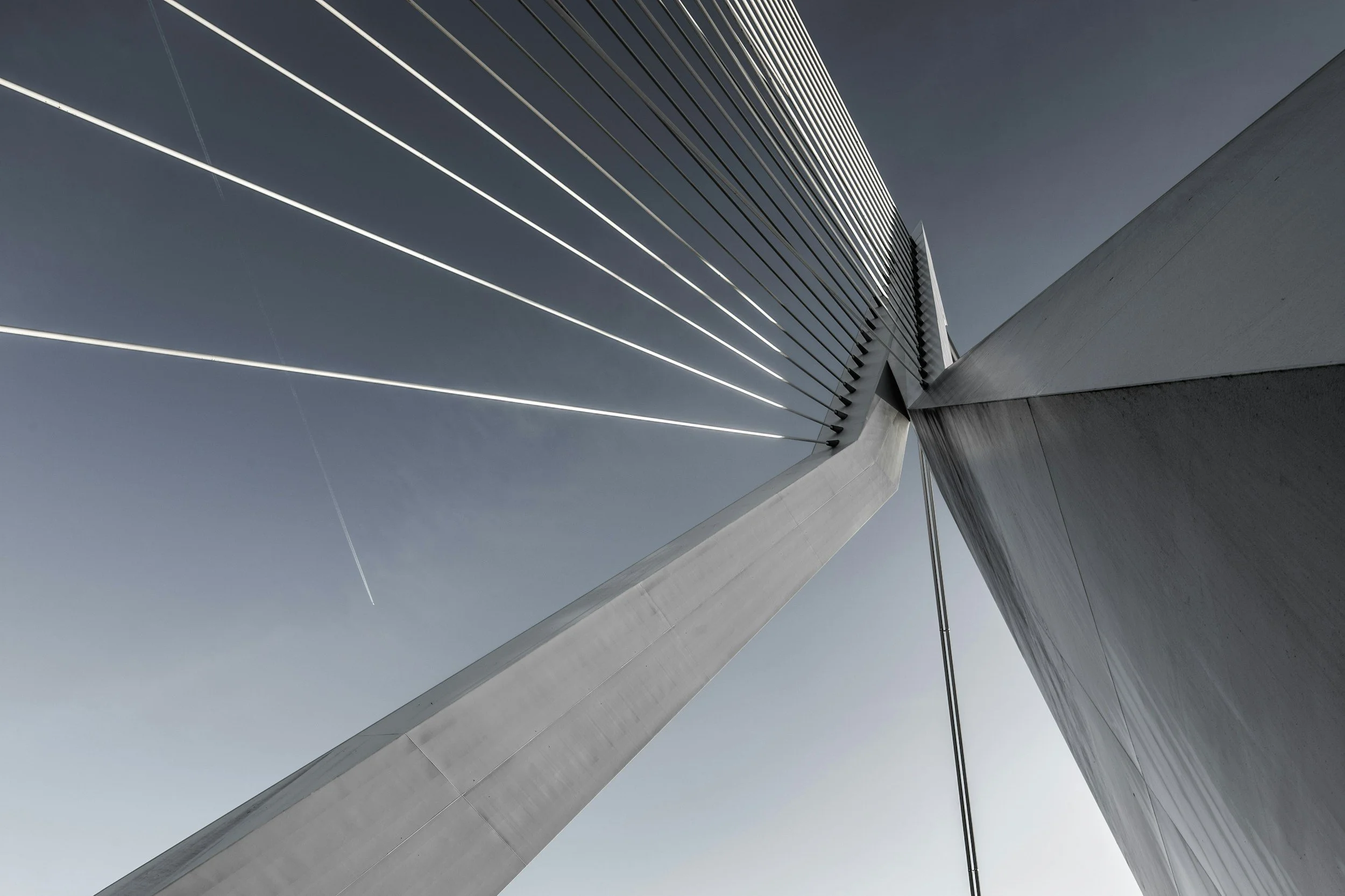 Low-angle view of a modern architectural building with curved, white concrete structures and horizontal, evenly spaced metal beams, against a clear grey sky.