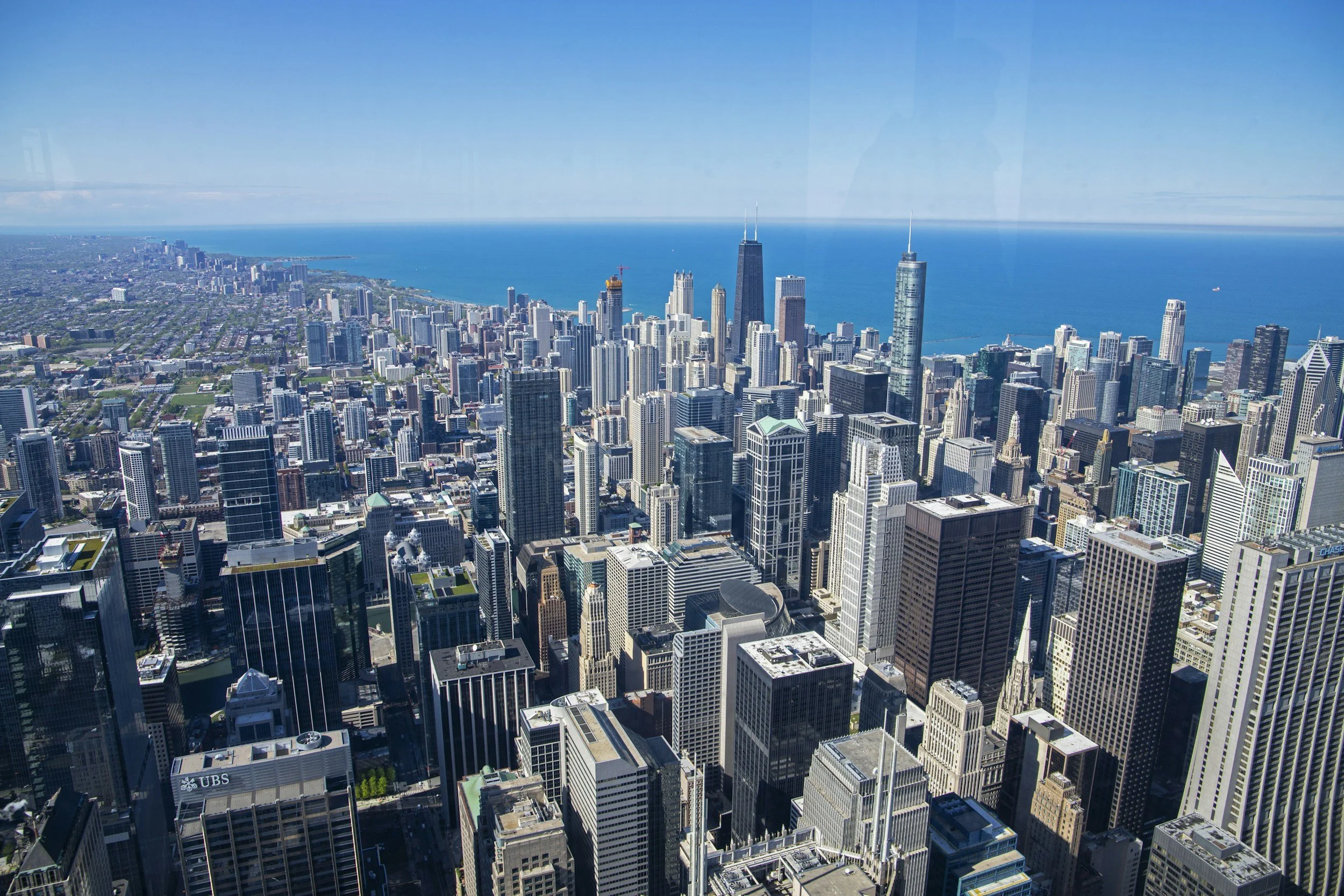 Aerial view of downtown Chicago, Illinois, featuring skyscrapers and Lake Michigan in the background on a clear, sunny day.