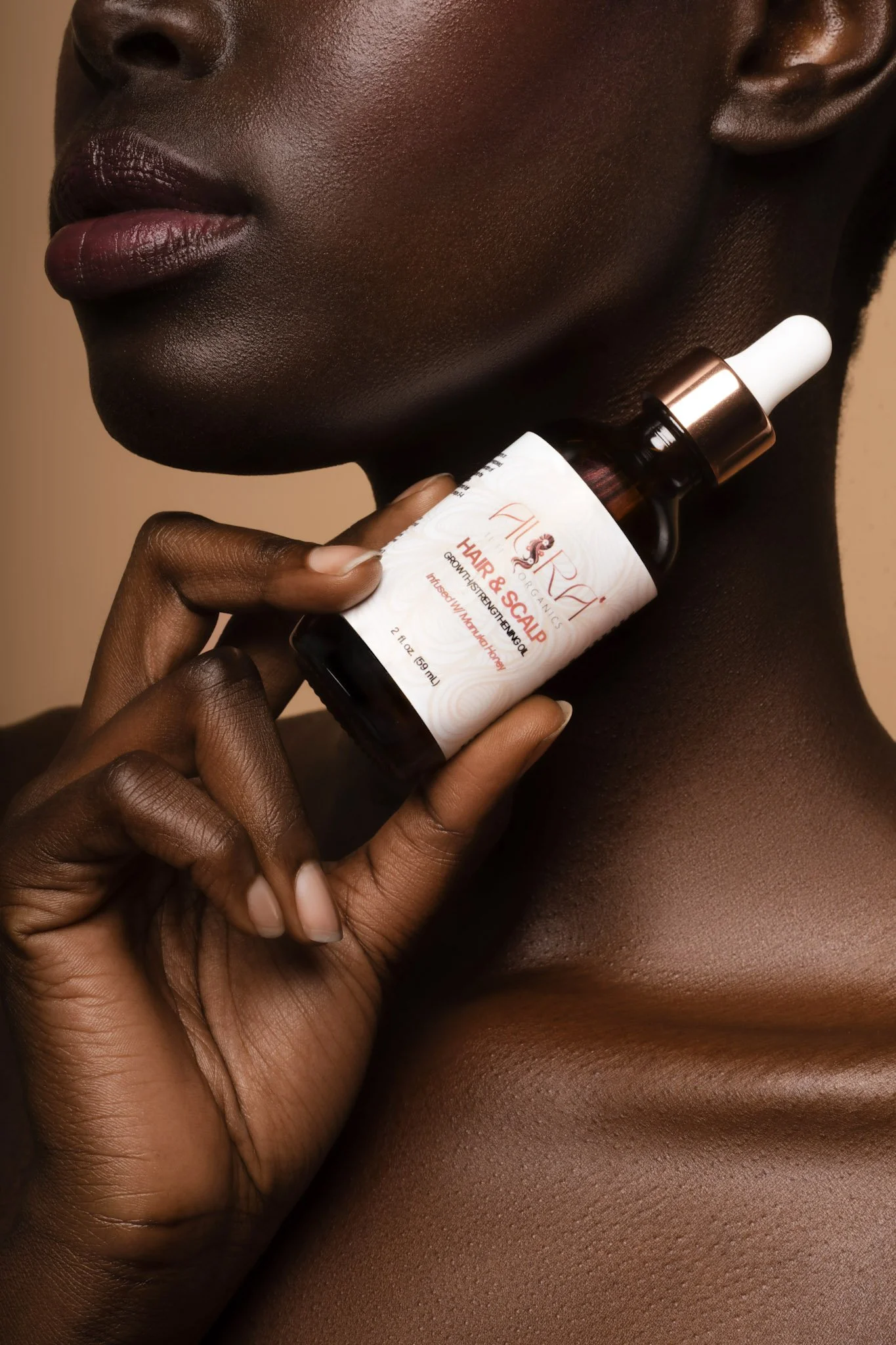 Close-up of a woman with dark skin holding a bottle of hair and scalp growth serum near her face.