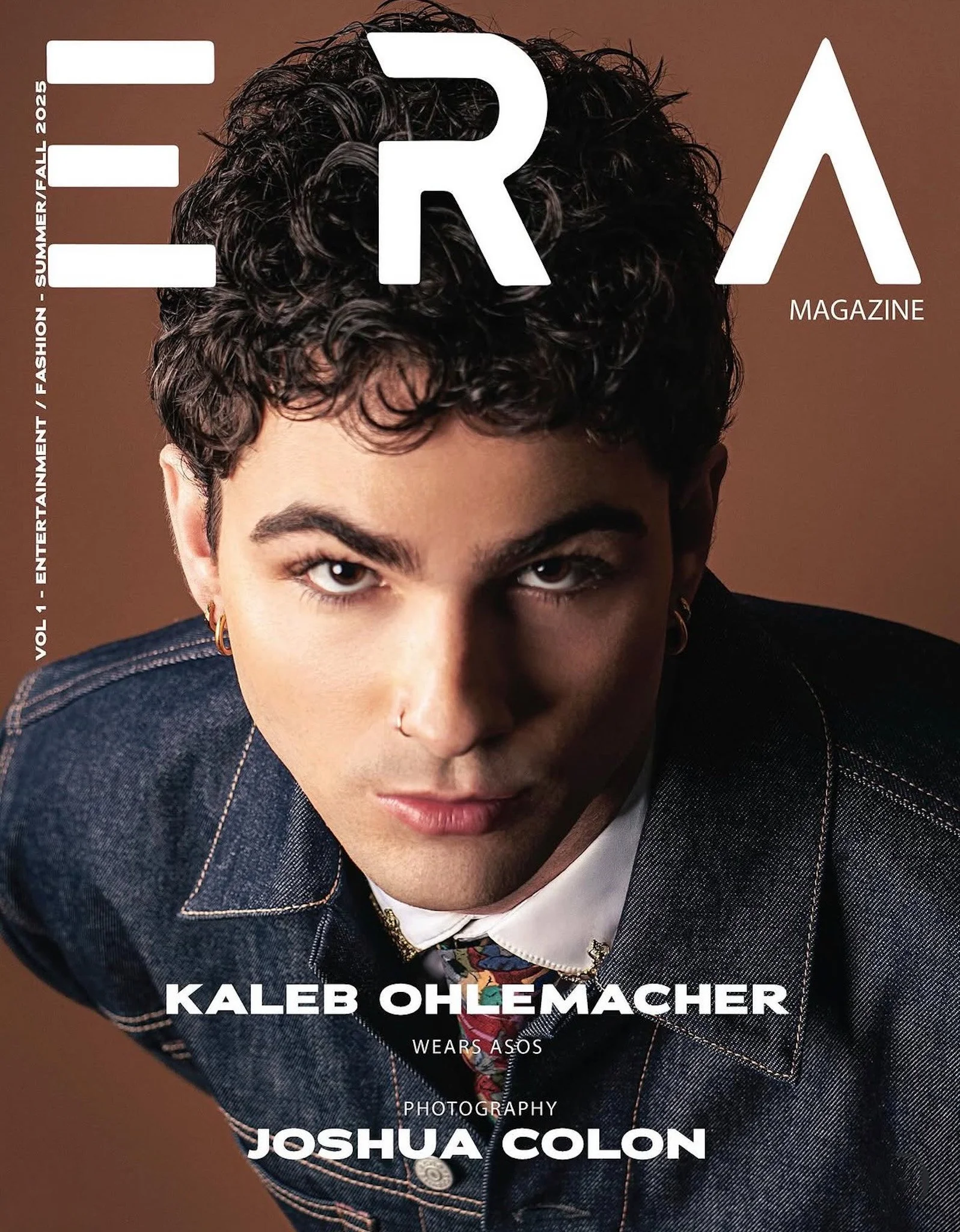 Close-up of a person with short curly hair, wearing a denim jacket, a white shirt, and accessorized with earrings and rings. The person has a serious expression and looks directly into the camera. The magazine cover features the name Kaleb Ohlemacher and other text indicating it is a fashion magazine.
