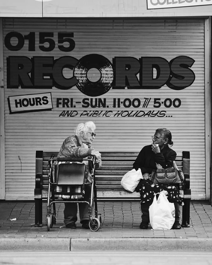 Two women on a bench talking  in front of a sign for "Records"