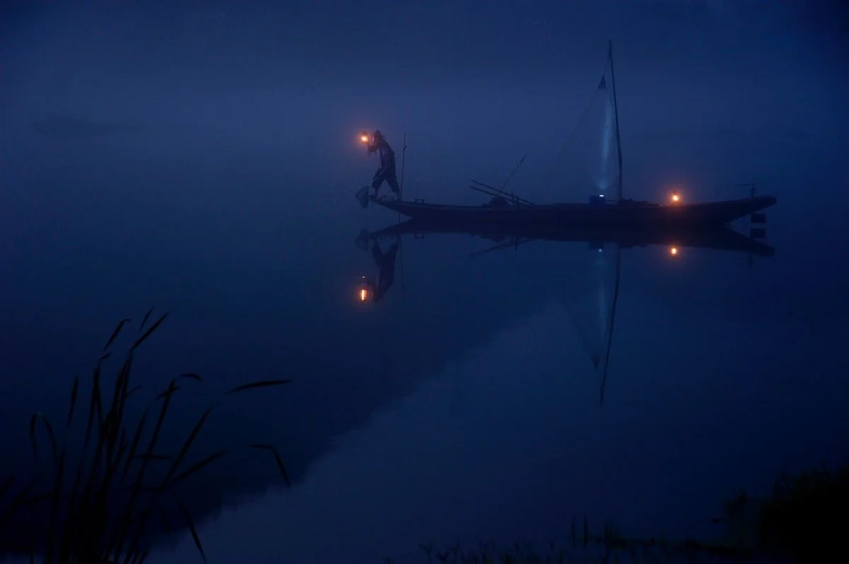 Man with a light on bow of a boat at night