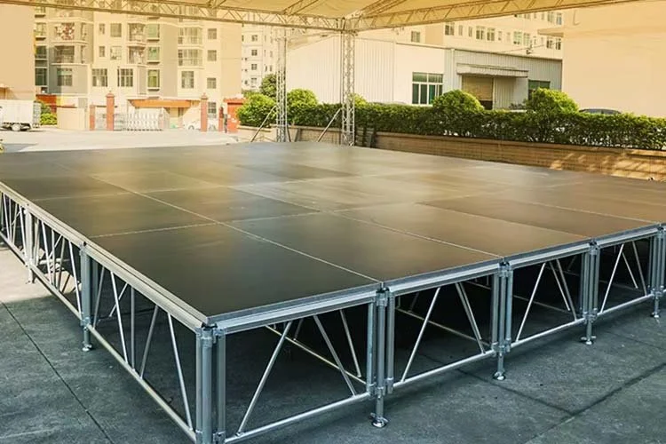 Temporary outdoor stage with black flooring on a rooftop, surrounded by city buildings and greenery in the background.