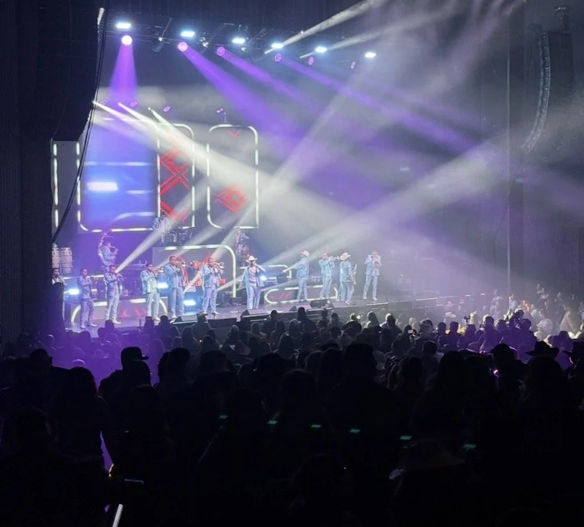A concert stage with performers and vibrant purple and blue lights, with an audience watching.
