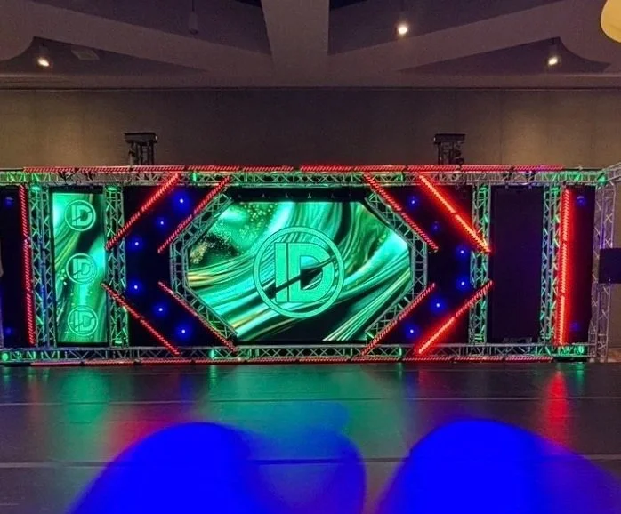 Colorful LED stage with a large central screen displaying a logo, flanked by vertical LED panels and red and green lighting accents.