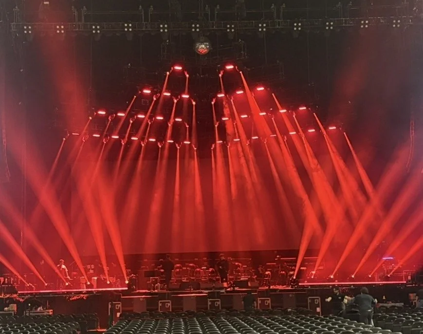 Concert stage with multiple red spotlights and fog, with empty seats in the foreground.