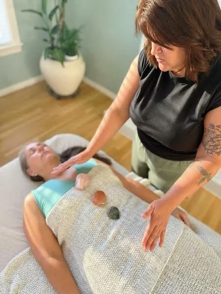 Jinae giving a Reiki healing session to a client lying on a massage table, with crystals placed on thire stomach.