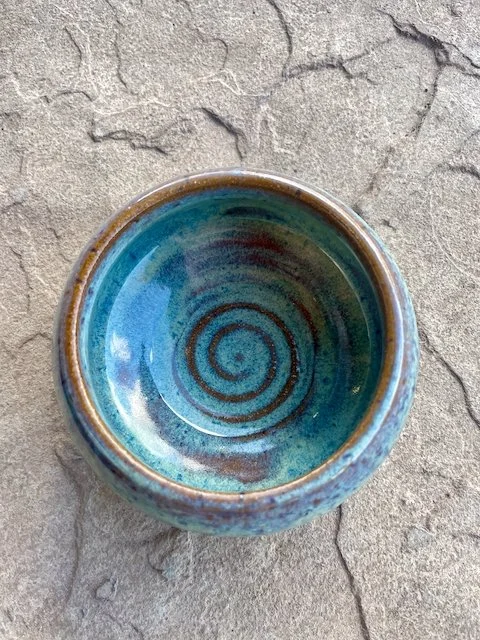 Ceramic bowl with a blue and green spiral pattern inside, placed on a cracked concrete surface.