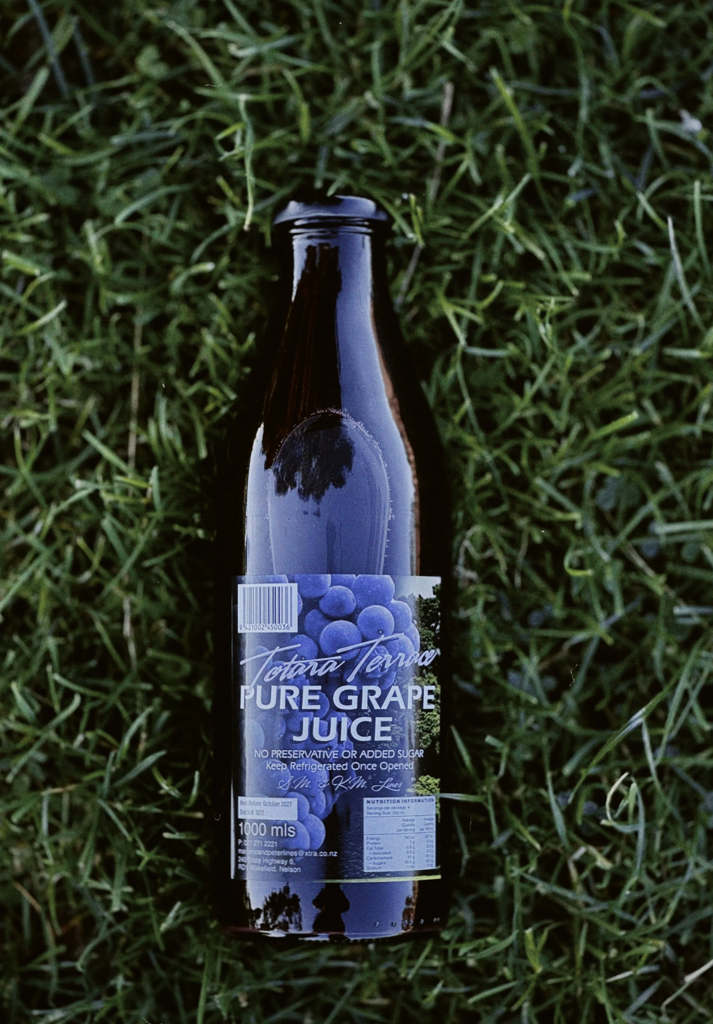 A bottle of Totara Terrace Pure Grape Juice lying on grass.