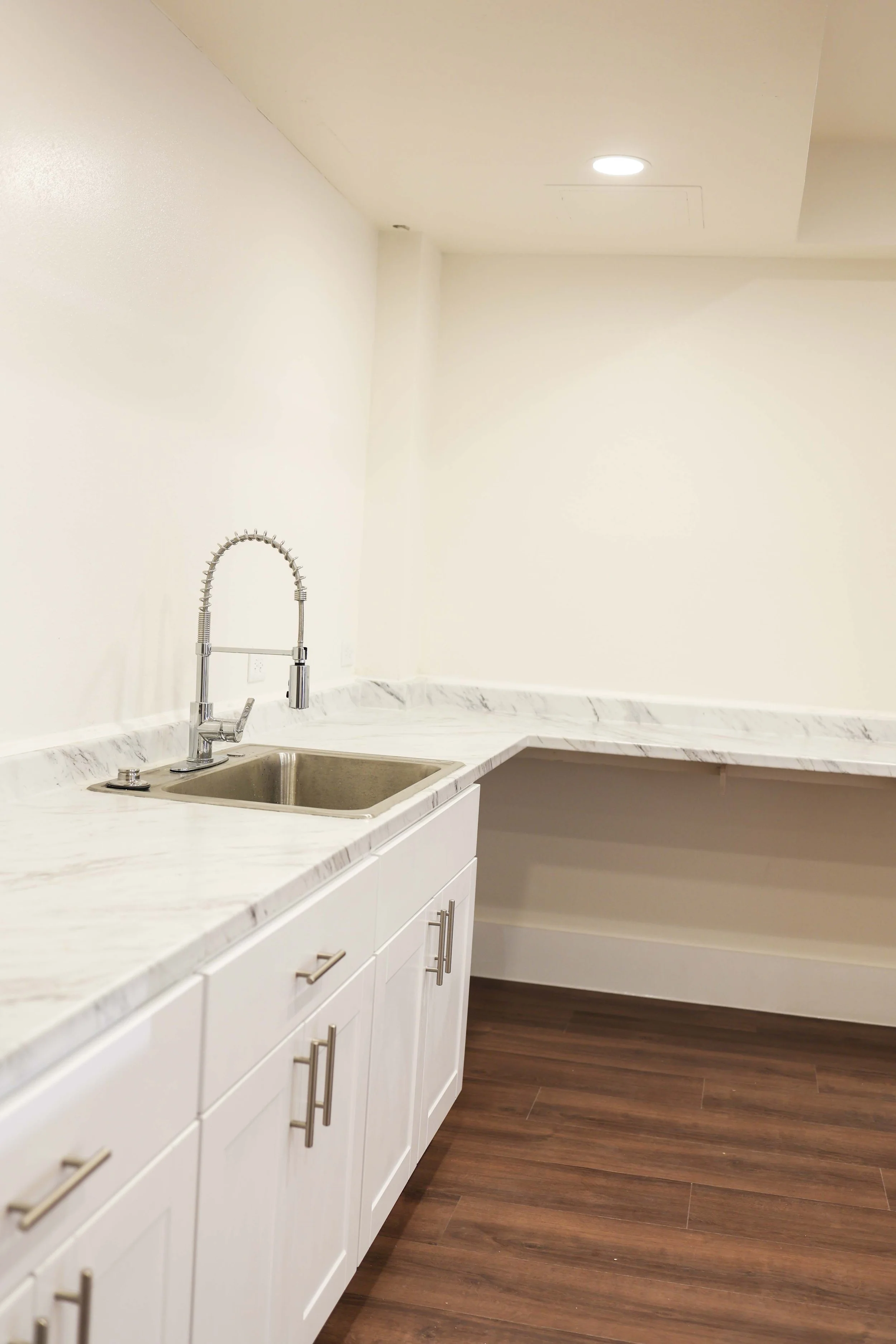 Kitchen countertop with white cabinets, marble pattern, stainless steel sink, modern faucet, and wooden flooring.