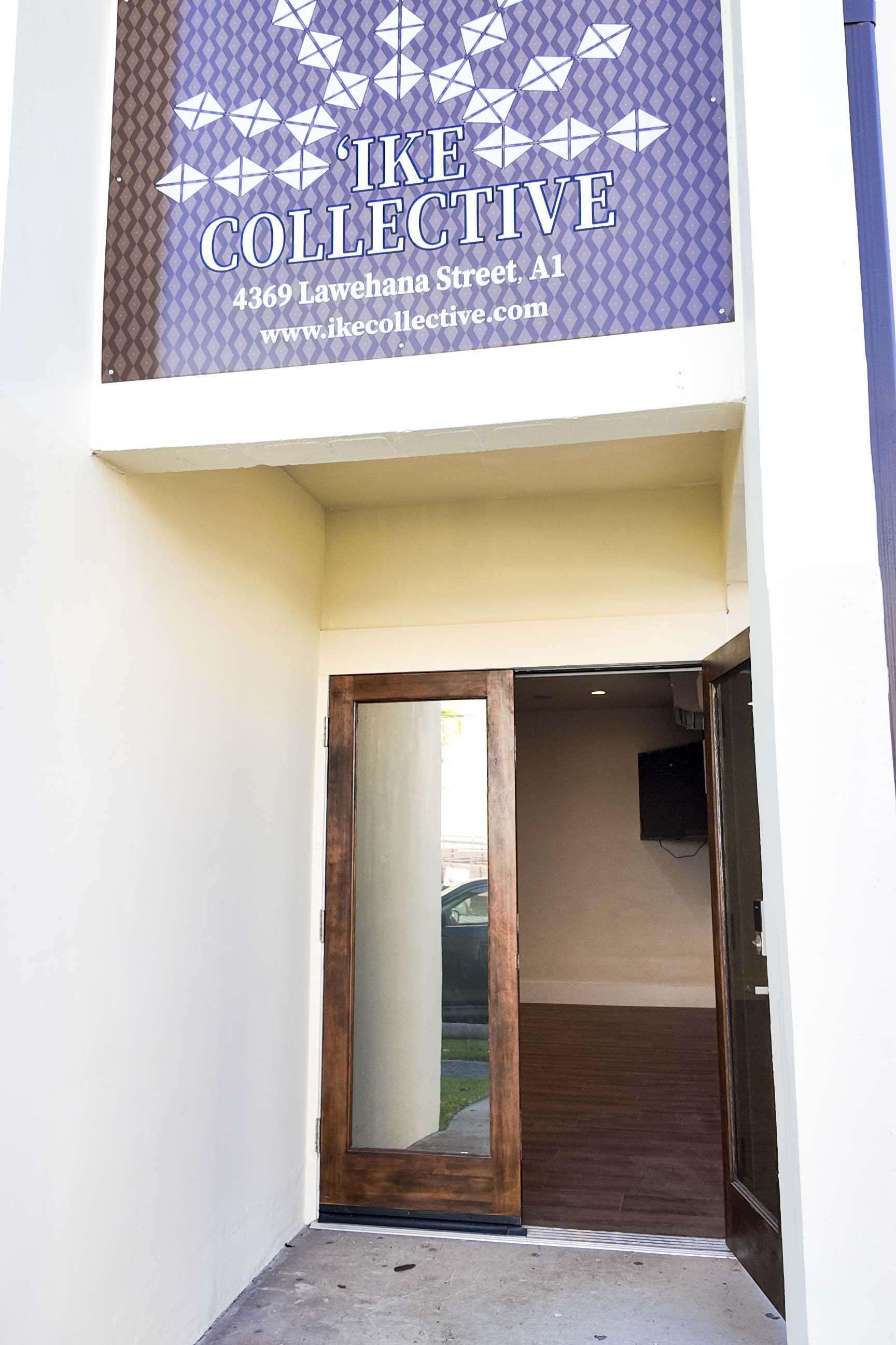 Storefront sign reading 'Ike Collective' at 4369 Lawehana Street, A1 with a website www.ikecollective.com. The entrance has a glass door with a wooden frame, and the interior is partially visible with an adjacent wall-mounted TV.