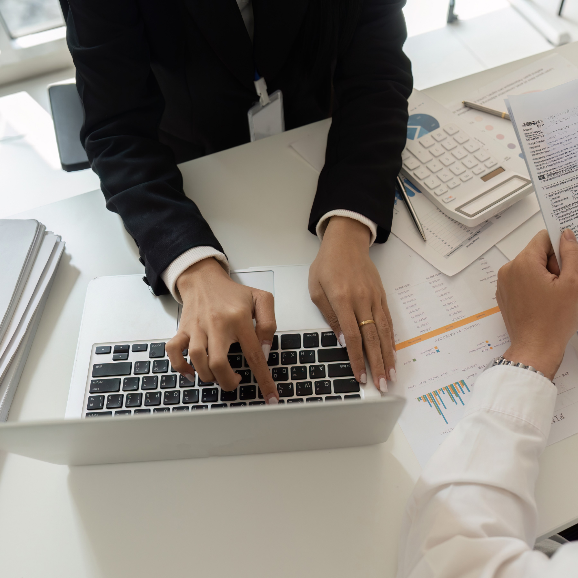 People working at a white desk with documents, a calculator, and a laptop