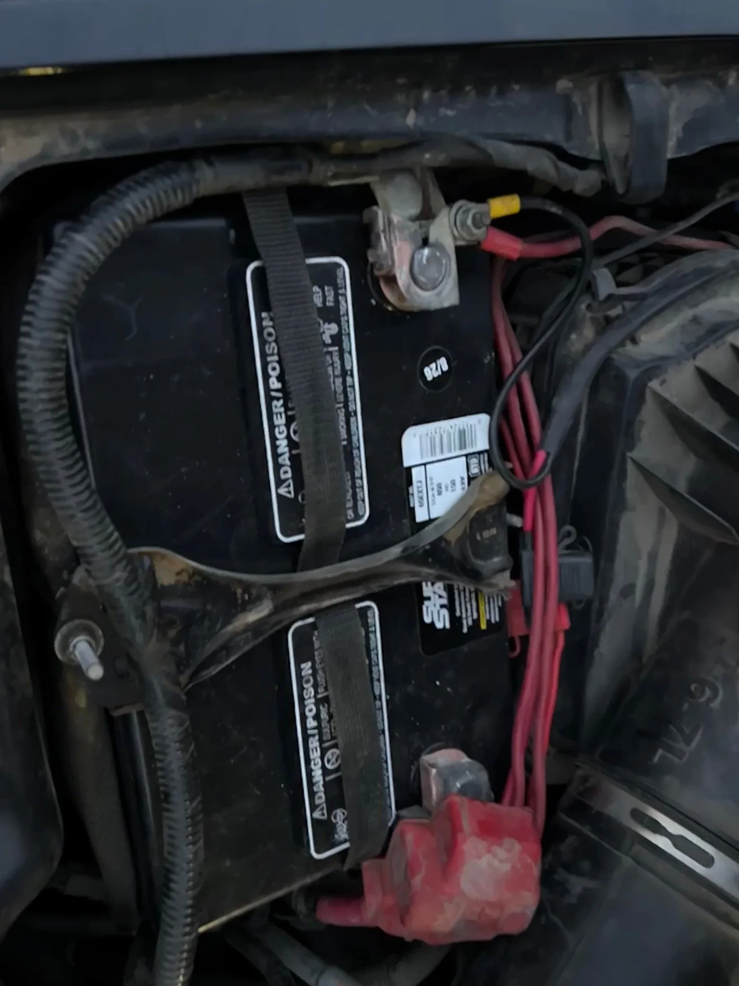 Car battery with cables connected, located in the engine compartment of a vehicle.