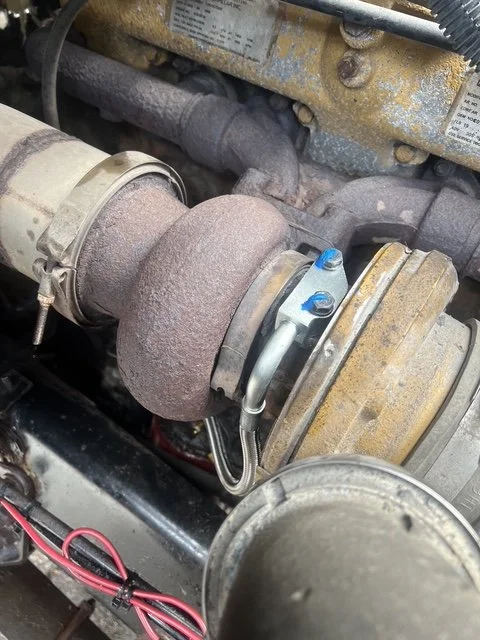 Close-up of a turbocharger and exhaust manifold in a vehicle engine, showing the rusty turbo components and connected pipes.